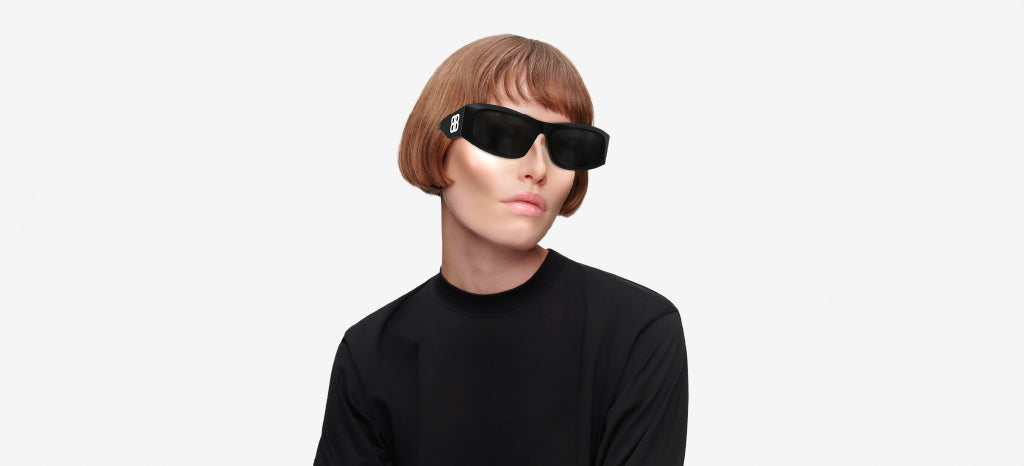 Person with short, straight, light brown hair and wearing black sunglasses and a black top, posing against a plain white background.