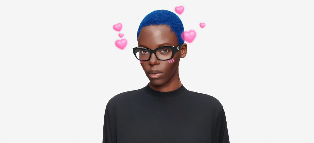 A person with bright blue hair and glasses wearing a black shirt, with pink heart emojis and blush marks added to their cheeks, set against a plain white background.