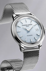 The Frederique Constant Classics Moneta Solarmetre FC-120LB3S6 wristwatch features a silver mesh band, light blue dial with metallic hour markers, and a date window at 3 o’clock—an elegant Swiss-made timepiece presented on a gray background.
