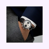 A person in a gray textured suit and navy blazer has their hand in their pocket, showcasing the Hamilton American Classic Intra-Matic Auto Chrono 40 mm Watch H38416711 by Hamilton Watches, featuring a panda dial and black leather strap.