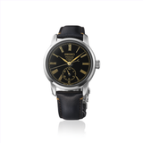 The Seiko Luxe Watches Presage Craftsmanship Series Enamel SPB499 showcases an elegant black enamel dial with gold Roman numerals, a small seconds subdial at 6 o’clock, a silver case, and a black leather strap. This refined timepiece from Seiko Luxe Watches is displayed against a plain white background.