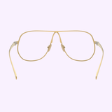 The Miu Miu 0MU Optical Frames 0MU A56S 5AK08N66 by Miu Miu Sunglasses feature gold wireframe pilot-style design with clear nose pads and slightly curved arms, shown against a light purple background.