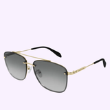 The Alexander McQueen AM0184SK 004 Men’s Sunglasses feature a gold-rimmed aviator design with black-tinted lenses and black ear tips, set against a light purple background—these luxury accessories from Alexander McQueen Sunglasses exude sophistication and make the ultimate statement piece.