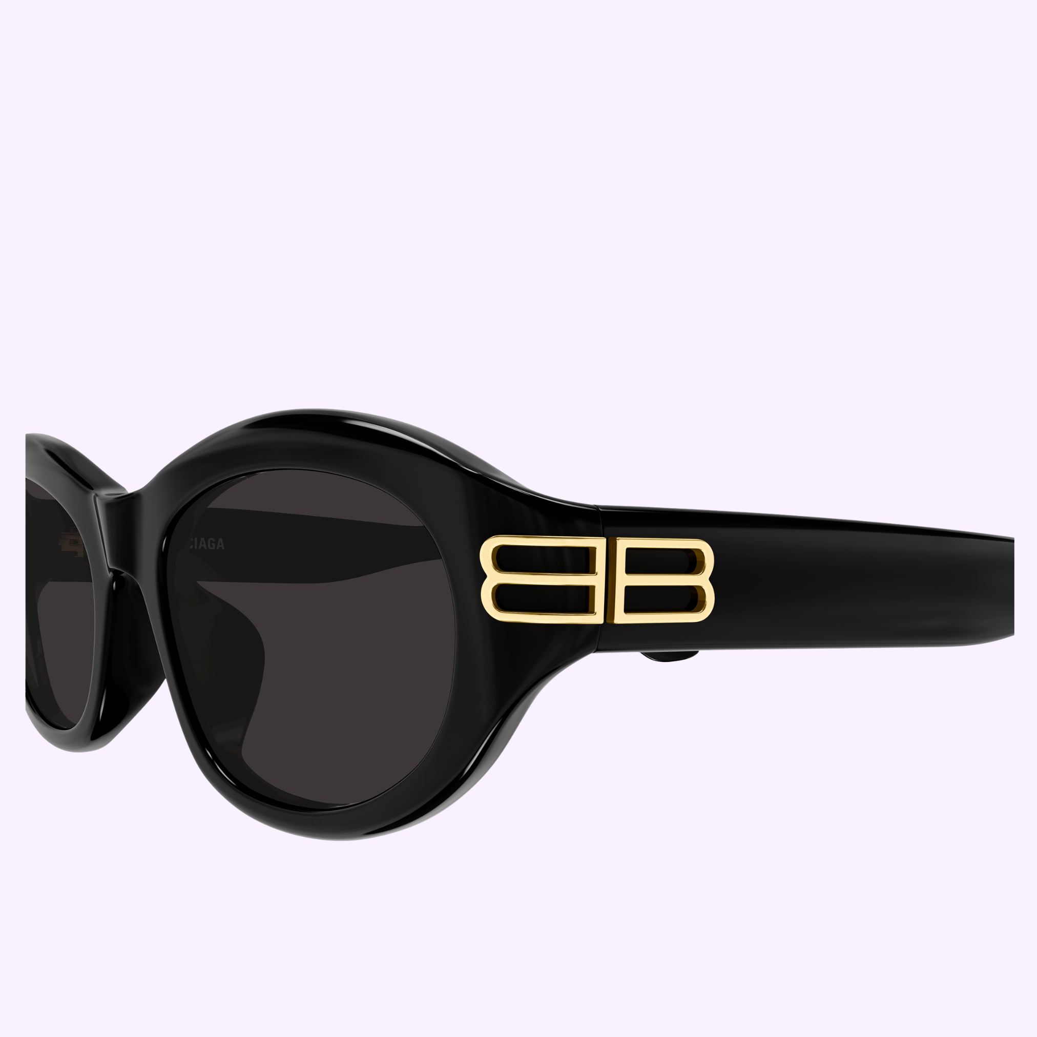 Balenciaga Sunglass BB0434SK-001 55, black oval frame with dark lenses and a gold double B logo on the temple, displayed on a light lavender background. Available from an Authorized Dealer in Miami.