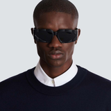 Wearing Balmain Sunglasses B-Spirit BPS-179A-56 Unisex, a person in a dark sweater over a white collared shirt stands against a light gray background, looking directly at the camera.