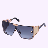The Balmain Sunglasses BPS-102N-146 Unisex feature large, square frames with blue-tinted lenses, gold accents, and textured gold side panels. A bold top bar and modern designer touches complete this standout look.
