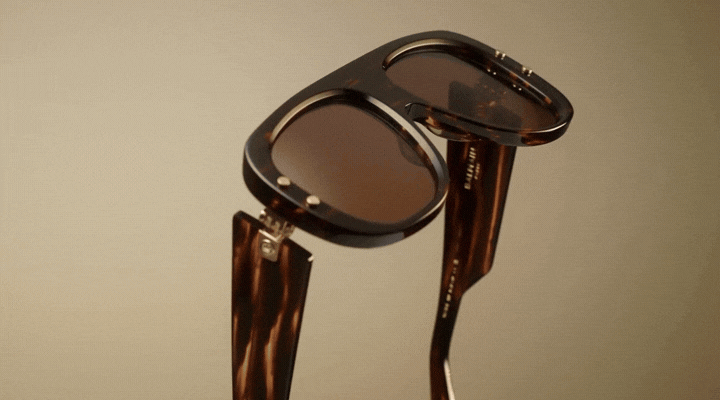 A pair of brown tortoiseshell sunglasses with flip-up lenses, demonstrating the movement as the dark lenses are lifted to reveal clear lenses underneath.