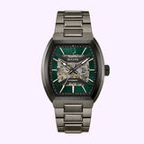 The Bulova Maquina 98A321 from Bulova Watches features a metallic band and a green and silver skeleton dial showcasing visible inner workings, displayed against a light pink background.