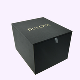 A black square box with BULOVA in gold on the lid, set on a plain light background—ideal for gifting the Bulova Watches Prestige Automatic 98A339 men’s watch in gold and silver-tone stainless steel.