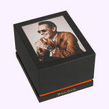 A black Bulova Watches box for the Surveyor Marc Anthony 97A205 features a lid image of a smiling man in sunglasses and tan jacket wearing the watch, plus a gold Bulova logo, gold-tone steel detail, and an orange accent stripe.