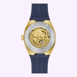 The image shows the back of the Bulova Watches Surveyor Marc Anthony 97A205, featuring a gold-tone stainless steel case, sapphire crystal, visible automatic movement, blue textured rubber strap, and engraved water resistance and model details.