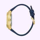 The Bulova Watches Surveyor Marc Anthony 97A205 features a thick gold-tone stainless steel case with a dark blue strap and buckle, showcased from the side against a pale light purple background.