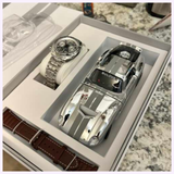 A Bulova Watches Shelby Daytona Coupe 96K118 Limited Edition silver watch, a matching silver sports car model with white stripes, and a brown leather watch strap are elegantly presented together in a gift box.