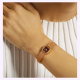 A vintage Bulova Watches Goddess of Time - Tiger’s Eye 97L185 watch with a rectangular tiger’s eye dial and a fine mesh gold-tone metal band worn on a wrist.
