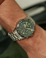 A close-up of a wrist wearing the Citizen Watches CA4664-60W Promaster Navihawk, featuring a green dial, silver stainless steel band, multiple subdials, detailed markers, rotating bezel, and sapphire crystal by Citizen Watches.