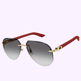 The Cartier CT0440S-003 61 Sunglass WOMAN METAL WOOD from Cartier Sunglasses features luxury aviator-style gold frames, gradient gray lenses, and red textured arms, shown on a light purple background.