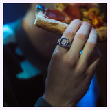 A person holds a slice of pepperoni pizza close to their mouth, highlighting their hand adorned with the G-Shock Watches CASIO RING WATCH CRW001-1 and a digital watch, set against a softly blurred background.