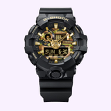 Introducing the CASIO G-Shock Watch Bold Camo Series GA700CF-1A by G-Shock Watches, featuring a striking black and gold camouflage design. This bold wristwatch combines analog and digital displays to present the time, day, and date. Its rugged look is highlighted against a light purple background.
