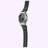 A CASIO G-Shock G-STEEL GM-2100-1ASW watch with a textured face and black rubber strap by G-Shock Watches, displayed vertically on a light lavender background.