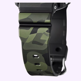 Close-up of a CASIO G-Shock Watch Bold Camo Series GA700CMG-3A strap by G-Shock Watches, showcasing its green and black camouflage pattern with two adjustment holes and a silver buckle, set against a light purple background—capturing the unique style of this iconic timepiece.