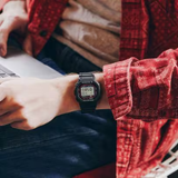 A person in a red patterned shirt uses a laptop, highlighting their G-Shock Watches CASIO G-Shock Watch DIGITAL DW5000R-1A on their wrist.