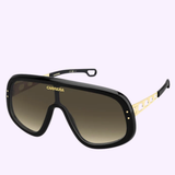 Carrera Sunglasses FLAGLAB 17 2M2 by Carrera Sunglasses in sleek black and gold, featuring a large single shield lens and cut-out accents on the gold arms, displayed against a light purple background.
