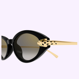Close-up of Cartier Sunglasses CT0634S-001 52: black cat-eye luxury eyewear with gold arms and a decorative leopard head near the hinge, shown against a light purple background.