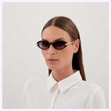 A person with straight brown hair, wearing Cartier Sunglasses CT0634S-001 52 and a white collared shirt, stands against a plain light background, showcasing luxury eyewear from Cartier.