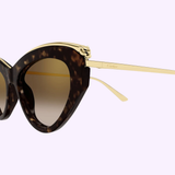 Cartier Sunglasses CT0596S-002 55 Women feature cat-eye tortoiseshell frames with gold accents and slim gold arms, embodying women's luxury eyewear style. Displayed against a light purple background. trust image