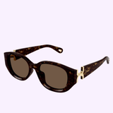 Tortoiseshell oval Chloe Sunglasses CH0237SK-002 54 feature dark lenses and gold accents on the arms, with the Chloe Sunglasses brand name engraved on the side. Blending classic elegance with contemporary style, these sunglasses are inspired by sporty pilot designs and make a versatile accessory for any woman’s look.