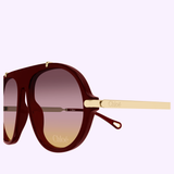 Chloe Sunglasses CH0357S-004 58 by Chloe Sunglasses in maroon and gold, featuring gradient lenses and a sporty pilot silhouette, displayed at an angle on a light lavender background.