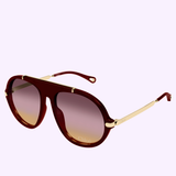 The Chloe Sunglasses CH0357S-004 58 by Chloe Sunglasses feature a burgundy oversized aviator frame, gold metal arms, and gradient brown-tinted lenses for a stylish modern twist on the Sporty Pilot look, showcased against a light background.