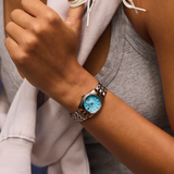 A silver stainless steel Citizen Watches Corso EW2291-51L analog watch with a light blue dial worn on a person’s wrist.