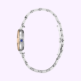 Side view of the Citizen Watches EM1136-87D L Mae, a women’s Eco-Drive with slim round two-tone case, silver metal link band, and blue-gem crown by Citizen Watches, shown on a light purple background. UPC: 013205166600.