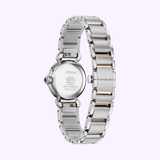 The back view of the Citizen Watches EM1136-87D Citizen L Mae (UPC 013205166600) highlights its stainless steel and gold-tone band, engraved details, and blue cabochon crown, set against a light purple background.