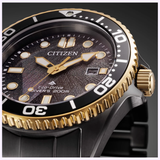 Close-up of the Citizen Watches Promaster Dive LIGHT in BLACK BN0264-53E with a textured black dial, gold-accented bezel and crown, bold hour markers, and a sleek black metal strap.