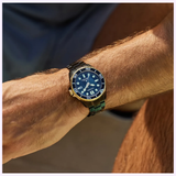 A close-up of a sunlit, tanned wrist wearing the Citizen Watches Promaster Dive LIGHT in BLACK BN0264-53E, featuring classic styling with a blue dial and bezel, silver and gold strap, and bold white hour markers.