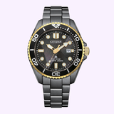 The Citizen Watches Promaster Dive LIGHT in BLACK BN0264-53E features Eco-Drive, a black and gold bezel, black dial with bold white markers, date at 3 o'clock, and a stainless steel bracelet—shown on a light purple background.