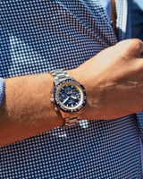 A Citizen Watches Promaster Navihawk CA4667-53L by Citizen Watches, featuring a stainless steel band and a dark blue multi-dial face, is worn on someone’s wrist. The person is dressed in a blue and white checkered shirt.