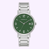 The Bulova 43A155 Caravelle Stainless Steel Strap Men Watch by Caravelle Watches By Bulova features a green dial, white hour markers, date at 3 o’clock, and metal link band, shown against a light purple background.