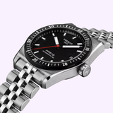 The Tissot Watches PR516 Powermatic 80 (T1494071105100, UPC: 7611608318492) features a black dial with silver markers, date display, stainless steel case and link bracelet, shown angled on a light purple background.