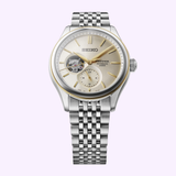 The Seiko Luxe Watches Presage Classic Series SPB480 features a silver automatic design with a metallic bracelet, gold accents, and an open-heart display on the left side, showcasing Japanese mechanical craftsmanship.