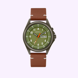 The Bulova 45C119 Classic Caravelle by Caravelle Watches By Bulova features a brown leather strap, olive green face, white hour markers, orange second hand, and day-date display against a light purple background. The Caravelle logo appears on the dial.