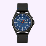 The Bulova 45C118 Classic Caravelle men's watch by Caravelle Watches By Bulova features a black leather strap, blue dial with white numerals, orange second hand, day-date display at 3 o’clock, shown on a light purple background.