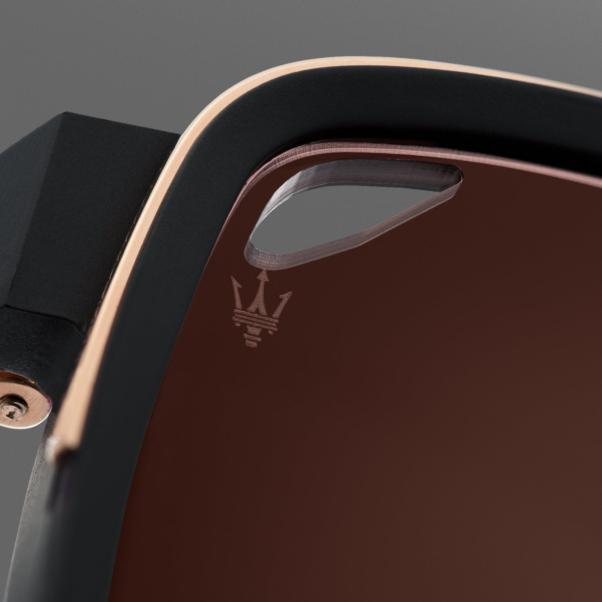 Close-up of the Dita Sunglasses Lancier and Maserati DLS333-A-01 by Dita Sunglasses, featuring a brown frame with a cutout, black edges, and a prominently displayed Maserati trident logo near the cutout; the luxurious performance design is highlighted by soft lighting and a blurred background.