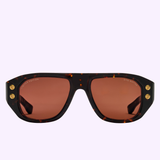 The Dita Sunglasses RHYTHX DTS741-A-03 Limited Edition features a sculptural navigator shape, brown rectangular lenses, and gold corner accents, presented against a light purple background.