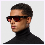 A man with short curly hair wears Dita Sunglasses RHYTHX DTS741-A-03 Limited Edition with red lenses and a black turtleneck, looking to the side against a plain light background.