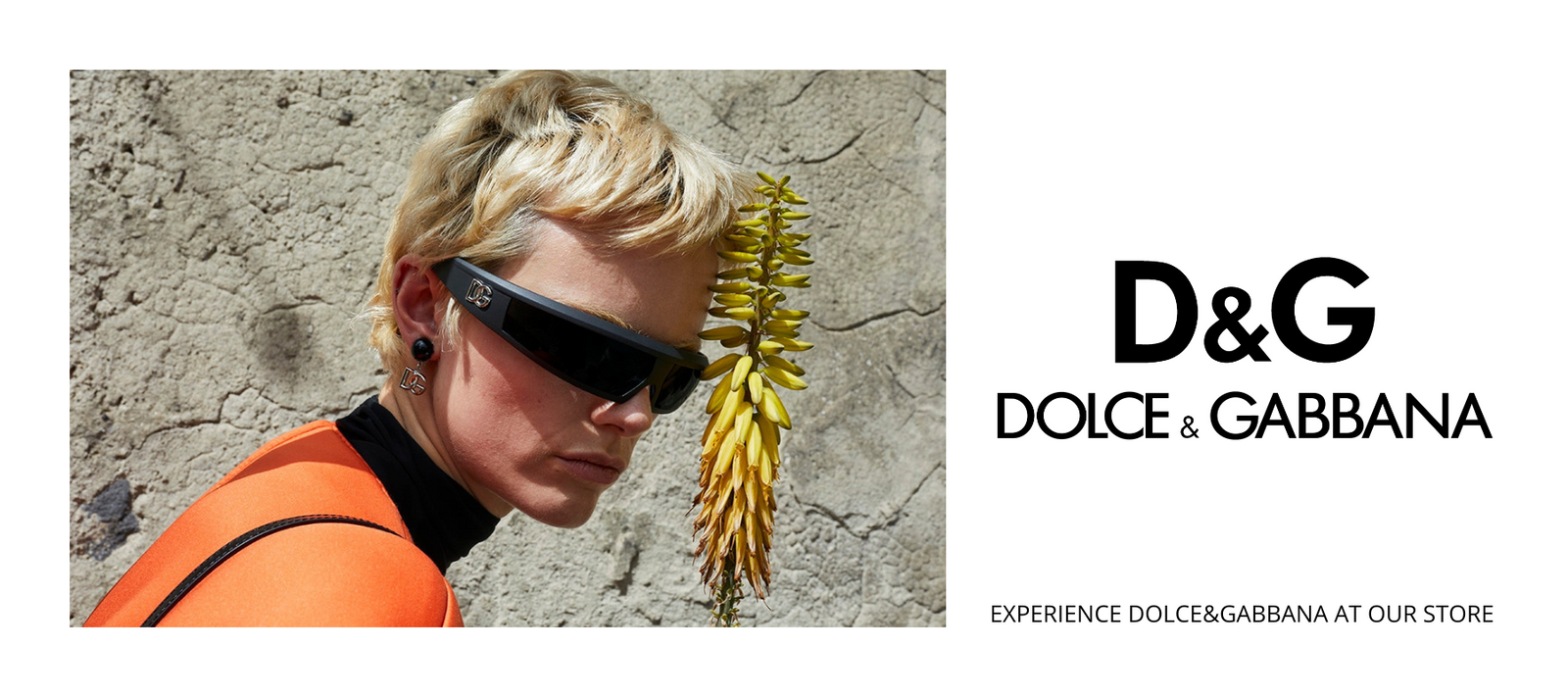 A person with short blond hair, wearing large black sunglasses and an orange top, poses beside a yellow flower against a textured concrete wall. D&G Dolce & Gabbana and a store invitation appear on the right.