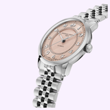 The Frederique Constant Classics Premiere FC-301SAL3B6B wristwatch features a stainless steel case, round pink dial with silver Arabic numerals, and a metal link bracelet, reflecting Geneva watchmaking elegance against a light purple backdrop.