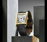 The Frederique Constant Carrée Small Seconds FC-235S2C5 wristwatch, featuring a gold rectangular case, a white dial adorned with black Roman numerals, and a sleek black leather strap, is showcased upright against a modern minimalist concrete backdrop. This refined timepiece from Frederique Constant’s Ladies Classic Carrée Small Seconds collection seamlessly combines timeless elegance with contemporary style.